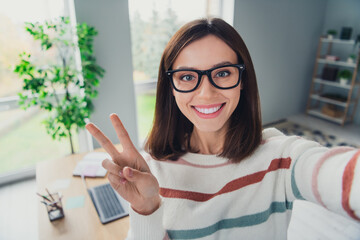 Wall Mural - Portrait of lovely cheerful lady beaming smile take selfie hand fingers demonstrate v-sign office inside