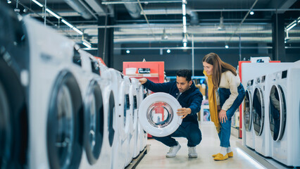 Wall Mural - Multicultural Couple Evaluates Washing Machine Choices at Home Electronics Store. Man and Woman in Search of a Reliable Laundry Appliance. Customers Explore Modern Laundry Solutions in Retail Shop