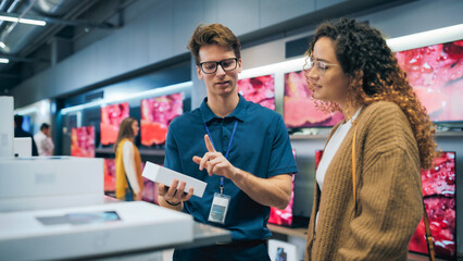 Wall Mural - Portrait of Female Customer Seeking Advice from Retail Home Electronics Expert. Hispanic Girl Explores Smartphone Options. Shopper Evaluating Latest Mobile Phone Innovations in the Department Store