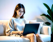 © anmitsu - Beautiful young Asian female freelancer is sitting on a comfortable sofa and browsing the internet on a laptop to successfully conduct business. Luxurious interior. Work from home concept.