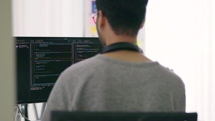 Wall Mural - a male developer with headphones around his neck is engrossed in coding, as seen on the monitor in f
