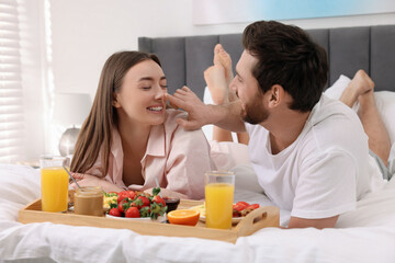 Wall Mural - Happy couple eating tasty breakfast on bed at home