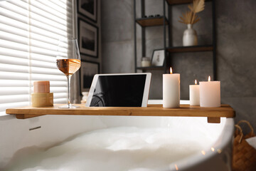 Poster - Wooden tray with tablet, wine, candles and toiletries on bathtub in bathroom