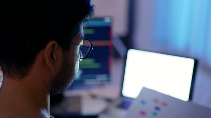 Wall Mural - a male programmer's profile is silhouetted against the backdrop of glowing screens during a focused 