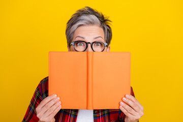 Poster - Portrait of aged lady hands hold book cover face eyes peek watch empty space ad isolated on yellow color background