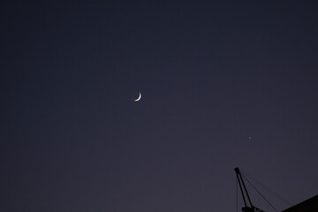 waning moon on blue sky at sunset, seen from a distance, not detailed