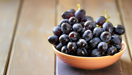 Poster - Bowl with a bunch of black grapes on wooden table; selective focus, bokeh, copy space