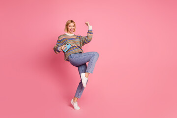 Full length photo of overjoyed woman dressed print sweater win bet scream yeah hold fist up smartphone isolated on pink color background