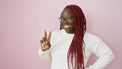 Canvas Print - A smiling woman with braids and glasses posing with a peace sign over a pink background