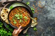 Traditional Indian Punjabi dish Dal makhani with lentils and beans in black bowl served with naan flat bread, fresh cilantro and two spoons on brown concrete rustic table top view. 