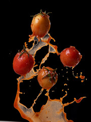 Wall Mural - tomatoes in red juice splash isolated on a black background