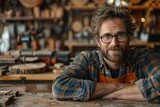 Fototapeta  - Friendly middle-aged craftsman posing in his woodworking workshop filled with tools and wood