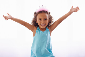 Little girl, excited and portrait on white background, princess crown and sweet for birthday and cute. Female child, kid and face for curly hair, happiness and joy for costume and playful in studio