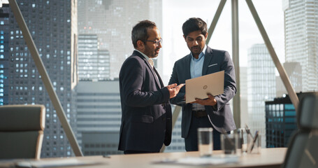 Aufkleber - Two Young South Asian Businessmen Standing Next to a Window in a Modern Office with a City Skyline View. Indian Managers Using Laptop Computer, Discussing Business Investments and Market Opportunities
