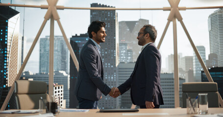 two young south asian businessmen shaking hands in a corporate office conference room. operations ma