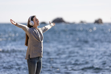 Wall Mural - Young woman standing, listening to music with arms outstretched, and breathing fresh sea air