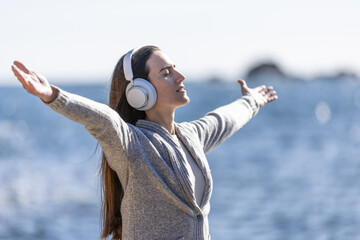 Wall Mural - Young woman listening to music with arms outstretched, and breathing fresh sea air