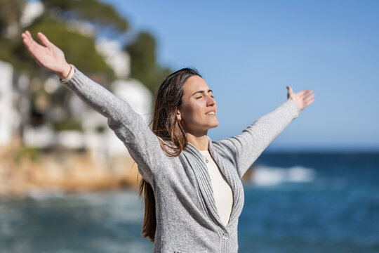 Smiling woman with arms outstretched on a beach, breathing fresh air.
