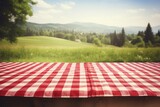 Fototapeta  - wooden table with a red checkered tablecloth on a blurred background with countryside. mockup picnic for the display of your product.