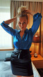 © Adriana - Young woman with blonde hair in a high bun, posing hands over her head in a hotel room, in Sweden. The woman is wearing black satin ankle-length pencil skirt, and a blue blouse. She is going out