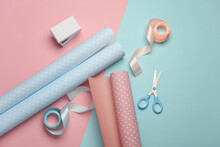 White Box With Satin Ribbons And Scissors, Rolls Of Wrapping Paper On Pastel Background. Holiday Concept. Flat Lay