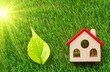 toy house model standing in green grass with a green leave, eco friendly concept, energy efficient solar powered housing