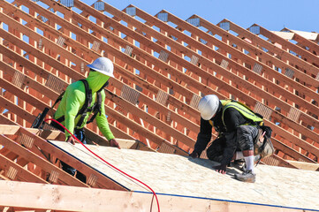 Construction workers installing the roof of a new wooden home by affixing plywood sheets using hand and power tools