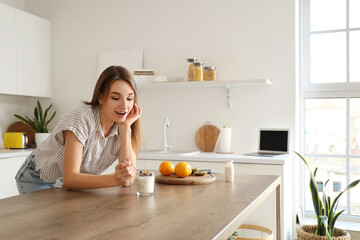 Poster - Young woman with tasty yoghurt in kitchen