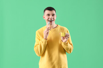Wall Mural - Young man with tasty yogurt and spoon on green background