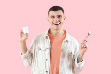 Wall Mural - Young man with tasty yogurt and spoon on pink background