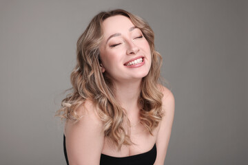 Wall Mural - Portrait of smiling woman with curly hair on grey background