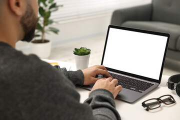 E-learning. Young man using laptop at white table indoors, closeup