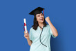 © Pixel-Shot - Happy female medical student in graduation hat with diploma on blue background