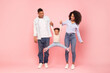 © Home-stock - Excited black family of three holding hands of little daughter, girl jumping in air over pink background in studio, parents and child having fun