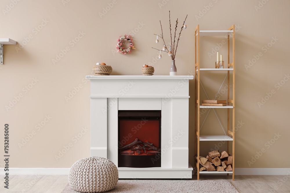 Vase with tree branches and Easter eggs on electric fireplace in interior of room