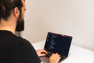 Professional software engineer, IT specialist, programmer, working at home and writing code on a laptop computer. A programmer works remotely at home on his laptop.