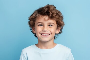 Wall Mural - Portrait of a smiling little boy with curly hair on blue background