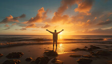 Man Standing On A Beach At Sunrise With His Arms At His Sides.