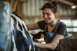 © Duckai - Cow farmer woman, milking a bovine animal inside a barn on a working woman's farm with copy space
