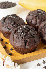 Wall Mural - Dark chocolate chip muffins with bananas on a wooden plate. Healthy sweet vegan dessert or snack. Close-up.
