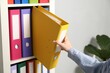 © New Africa - Woman taking binder office folder from shelving unit indoors, closeup
