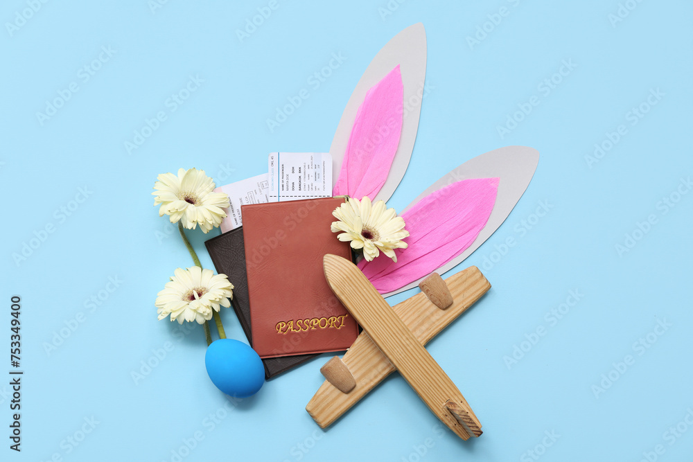 Passports with tickets, toy plane and Easter decor on blue background. Holiday travel composition