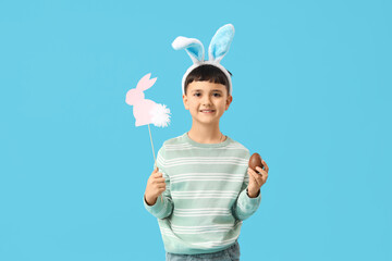 Sticker - Cute little boy in bunny ears headband with chocolate egg and decor for Easter on blue background