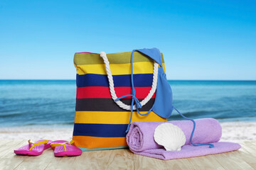 Sticker - Stylish striped bag and other beach accessories on wooden table near sea