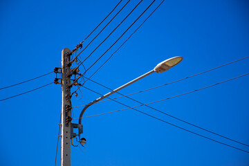 Electric pole with many wires and a road light. Blue sky background.