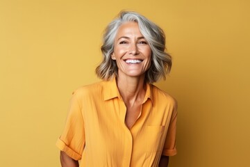 Wall Mural - Portrait of a happy senior woman smiling at the camera over yellow background