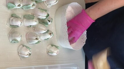 Wall Mural - A woman sprinkles powdered sugar on marshmallow lilies. Homemade marshmallows. Vertical video.