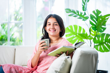 Wall Mural - Pretty Indian young girl reading book or novel at home