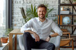 © Ishra - Portrait of a smiling businessman sitting inside minimal workplace, professional confident looking young man seated in office, Business man working in modern office room, The CEO sits in office chair