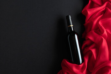 Wall Mural - Bottle of red wine with red satin on a black background.